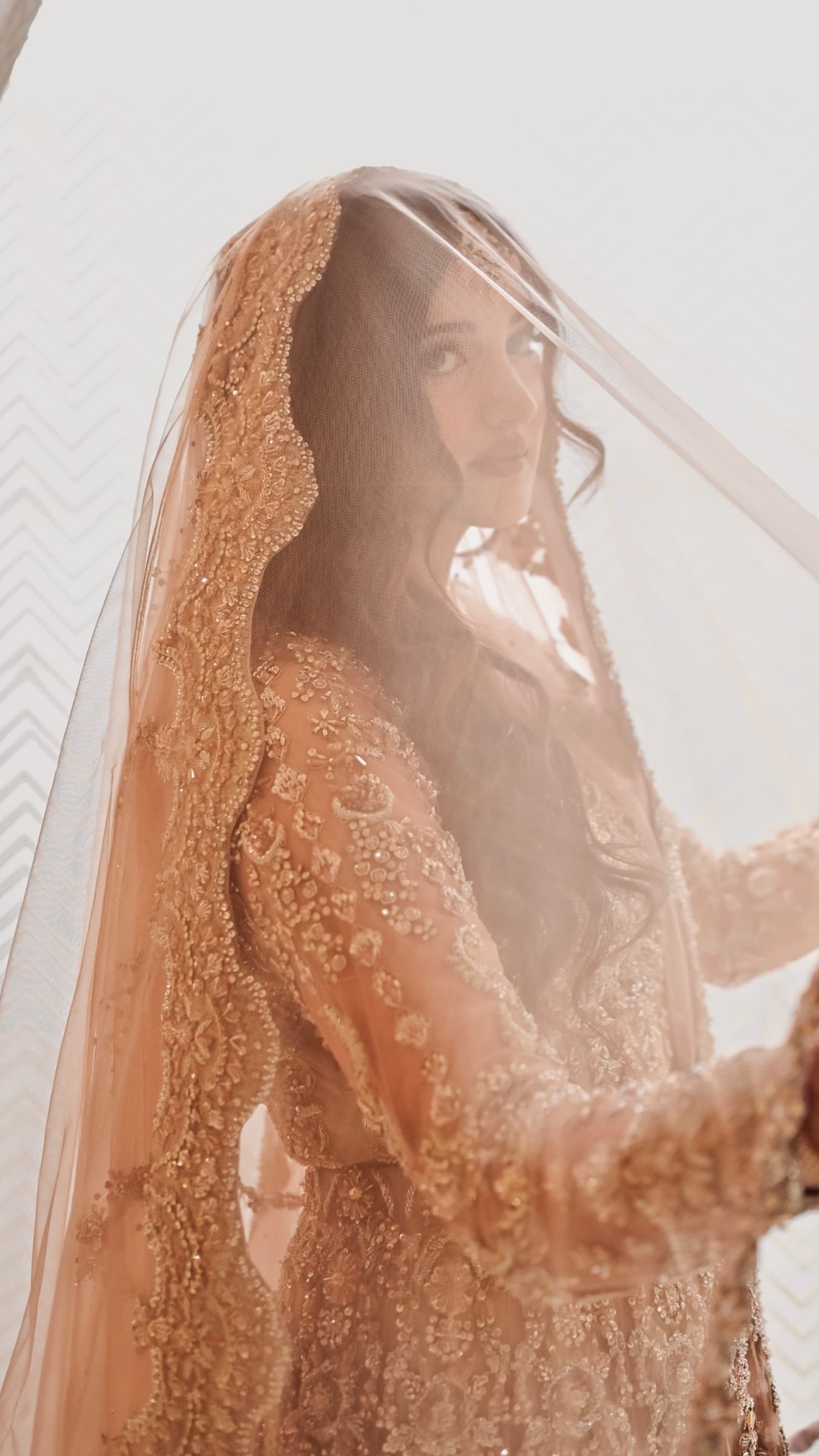 Bride in a champagne crystal-embellished gown and veil by a window — nikkah makeup and hair