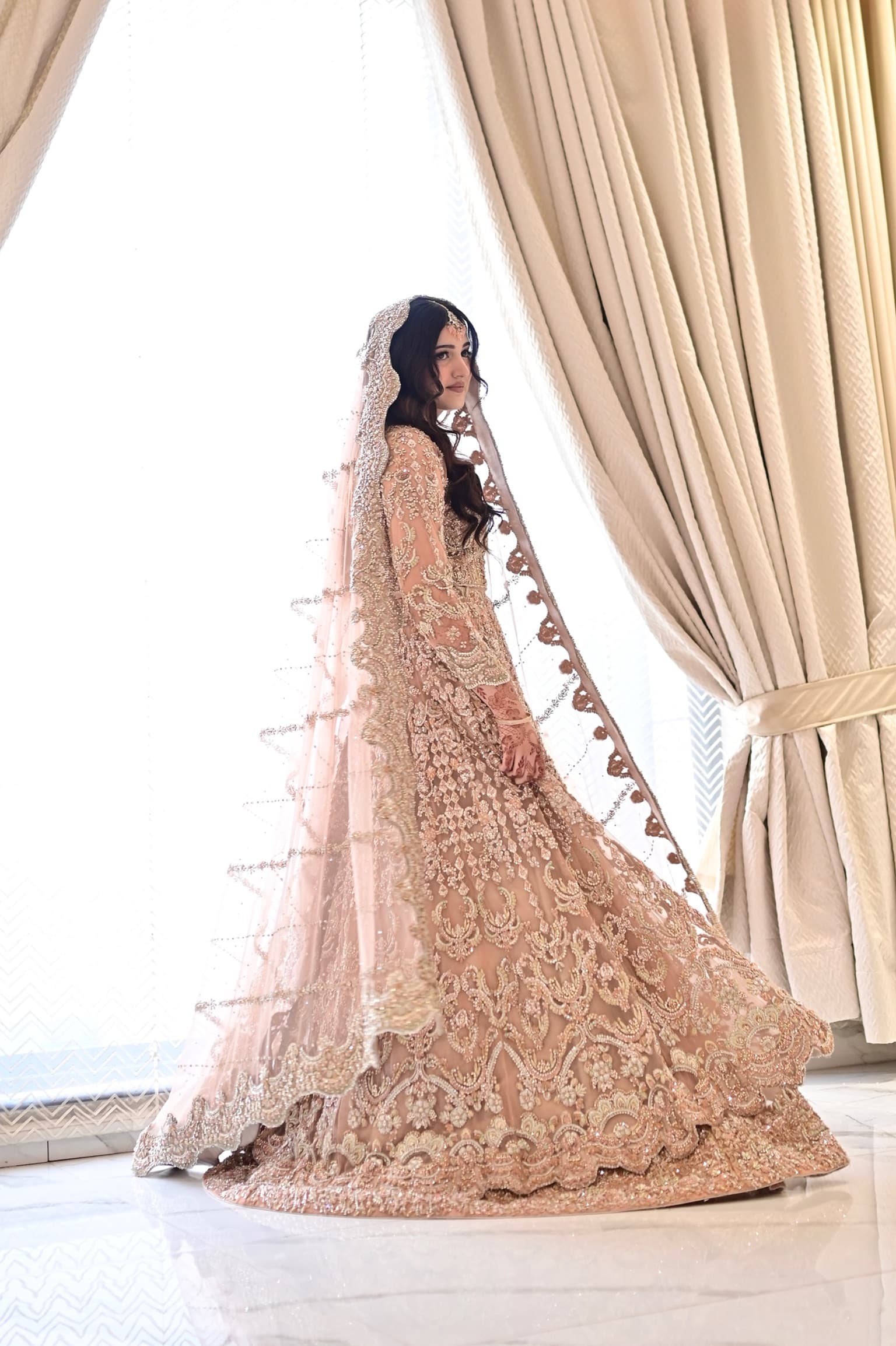 Bride in a champagne crystal-embellished gown and veil by a window — nikkah makeup and hair