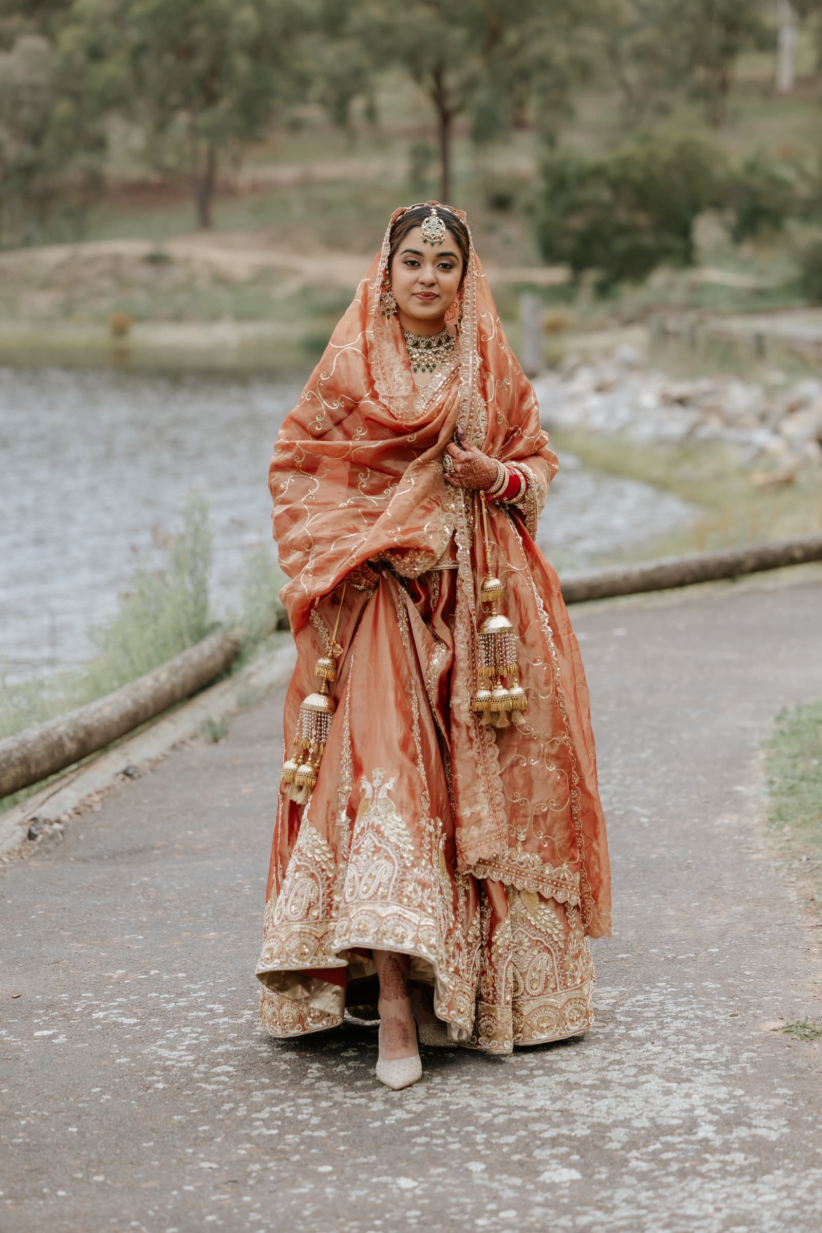 Bride in a rust-orange and gold embroidered bridal lehenga. 