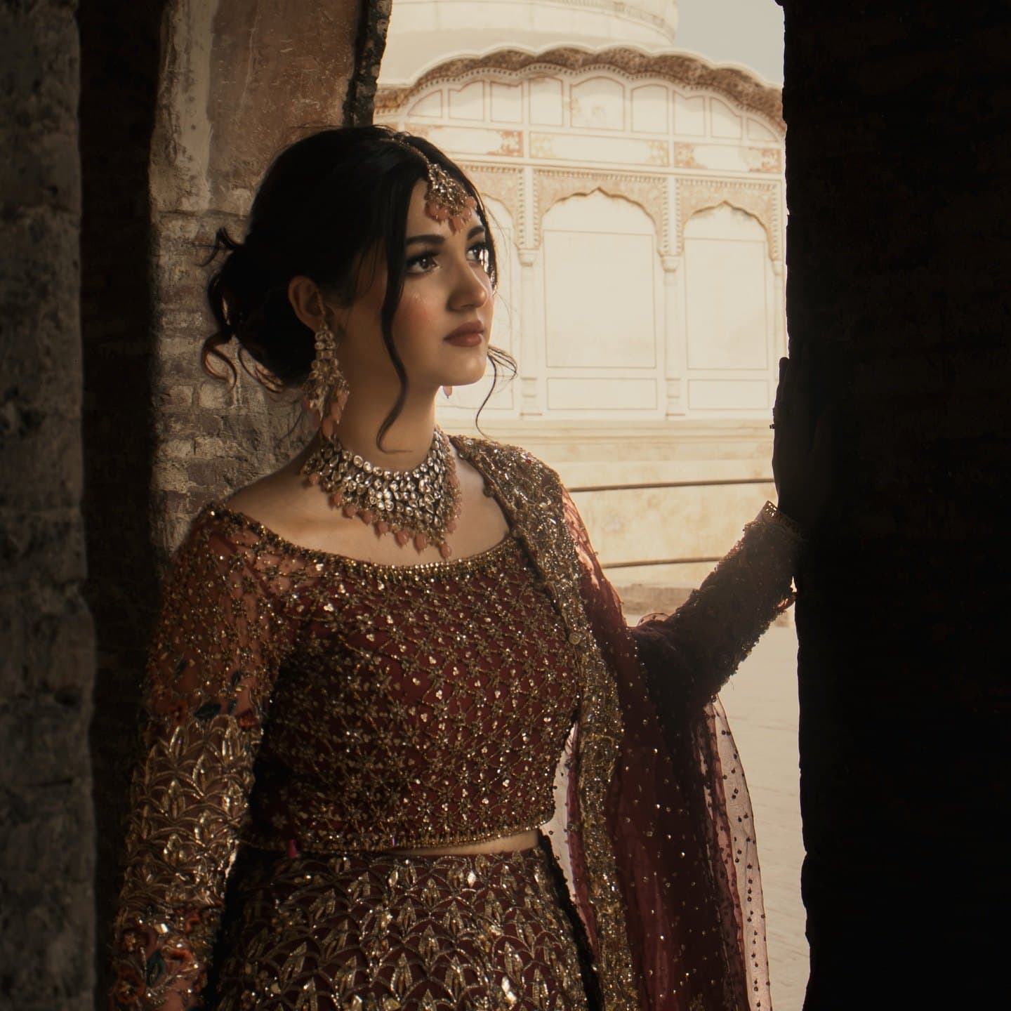 Bride in a maroon and gold lehenga at a heritage fort — bridal makeup and hair by Shelly Bhandari
