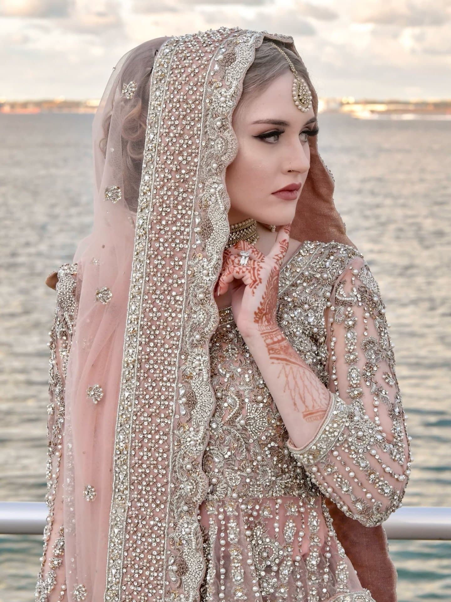 Bride in a blush, pearl-embroidered gown by the water at sunset — engagement makeup and hair